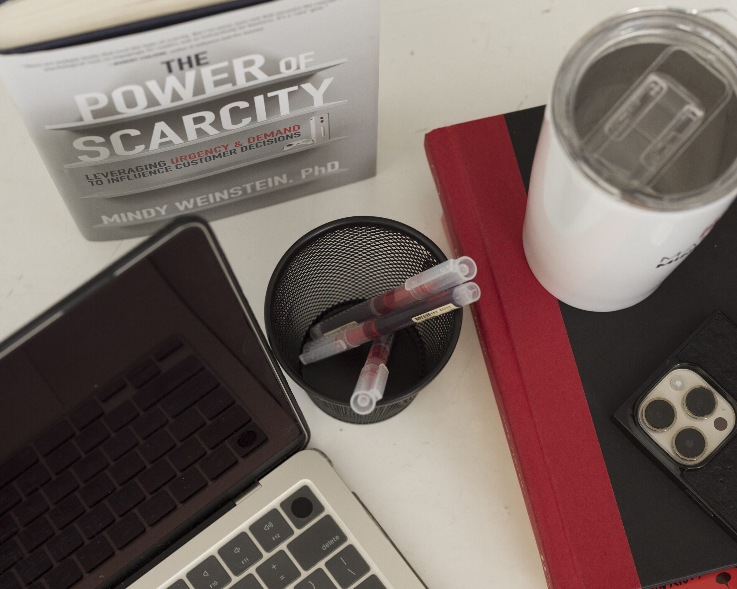 view of office items, laptop, phone, cup, and book sitting on a desk