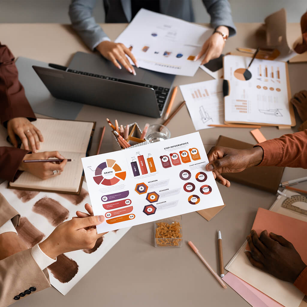 Team collaborating around a table with charts, infographics, and laptops, discussing marketing analytics and strategy using colorful data visualizations.